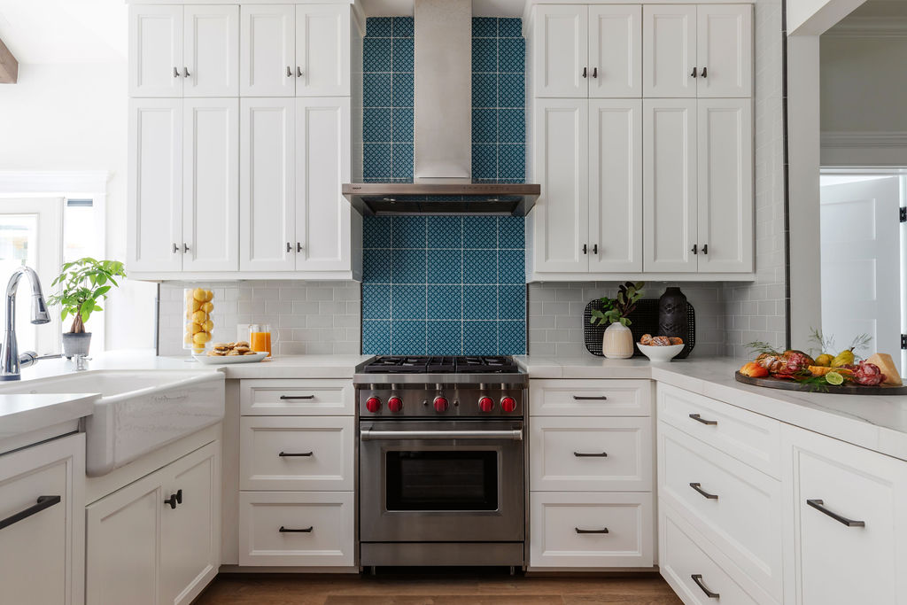 Modern kitchen with white shaker-style cabinets, a bold blue tiled backsplash, stainless steel Wolf gas range and hood, Neolith Mont Blanc Silk countertops, and European White Oak flooring; natural light fills the space from the left side.