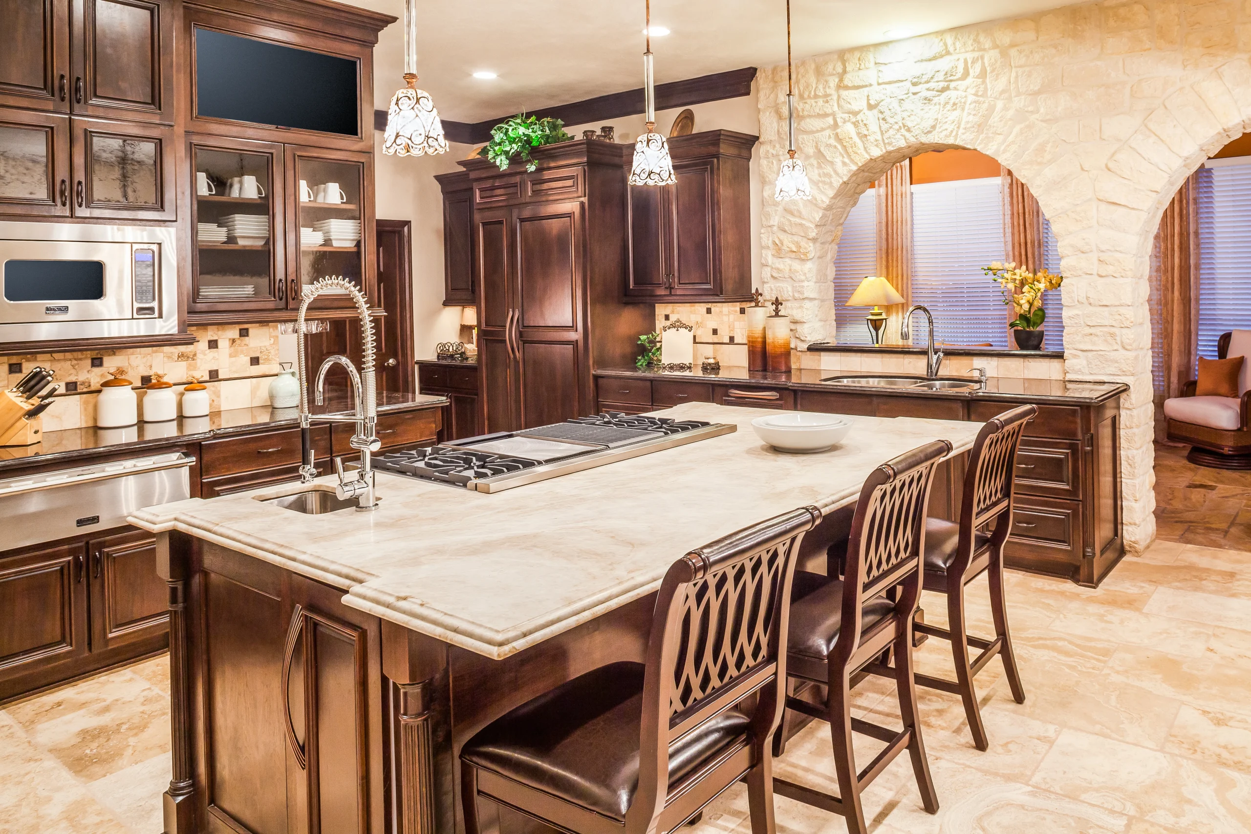 A modern kitchen with light wood cabinetry, white marble countertops, a large central island with bar stools, and pendant lighting overhead. Stainless steel appliances and an open floor plan create a bright, airy, and contemporary feel.
