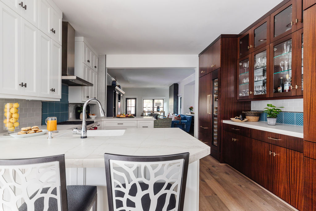Spacious kitchen featuring a white island with integrated sink, modern barstools, white and stained mahogany cabinetry, Neolith Mont Blanc countertops, glass-front upper cabinets, and LV6 European White Oak flooring extending into the open living area.